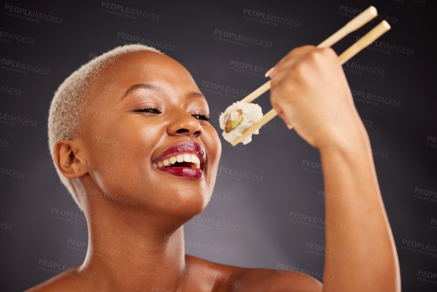 Buy stock photo Face, eating and woman with sushi and chopsticks in studio for healthy food or beauty. Black female model with makeup on a dark background for wellness glow, fish diet or seafood with nutrition
