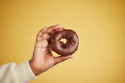 Buy stock photo Hand, donut and chocolate dessert in studio for unhealthy eating, sugar or cake advertising. Closeup of a person with a doughnut on a yellow background for junk food, diet calories or fun emoji