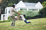 Family, children and a father spinning his son around in the garden of their home while playing together. Kids, yard and bonding with a happy boy child having fun with his dad on grass outdoor