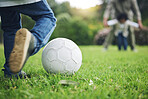 Child, legs and kick soccer ball on grass for fun activity, childhood or playing in the park. Playful little boy in sports game or match for score, point or goal on green field in the nature outdoors