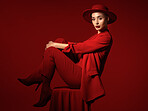 Portrait, fashion and a woman on a chair in studio on a red background for elegant or trendy style. Aesthetic, art and beauty with a young female person sitting in an edgy, classy or unique suit