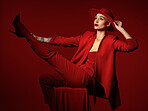 Vision, fashion and a woman on a chair in studio on a red background for elegant or trendy style. Thinking, art and beauty with a young female person sitting in an edgy, classy or unique suit