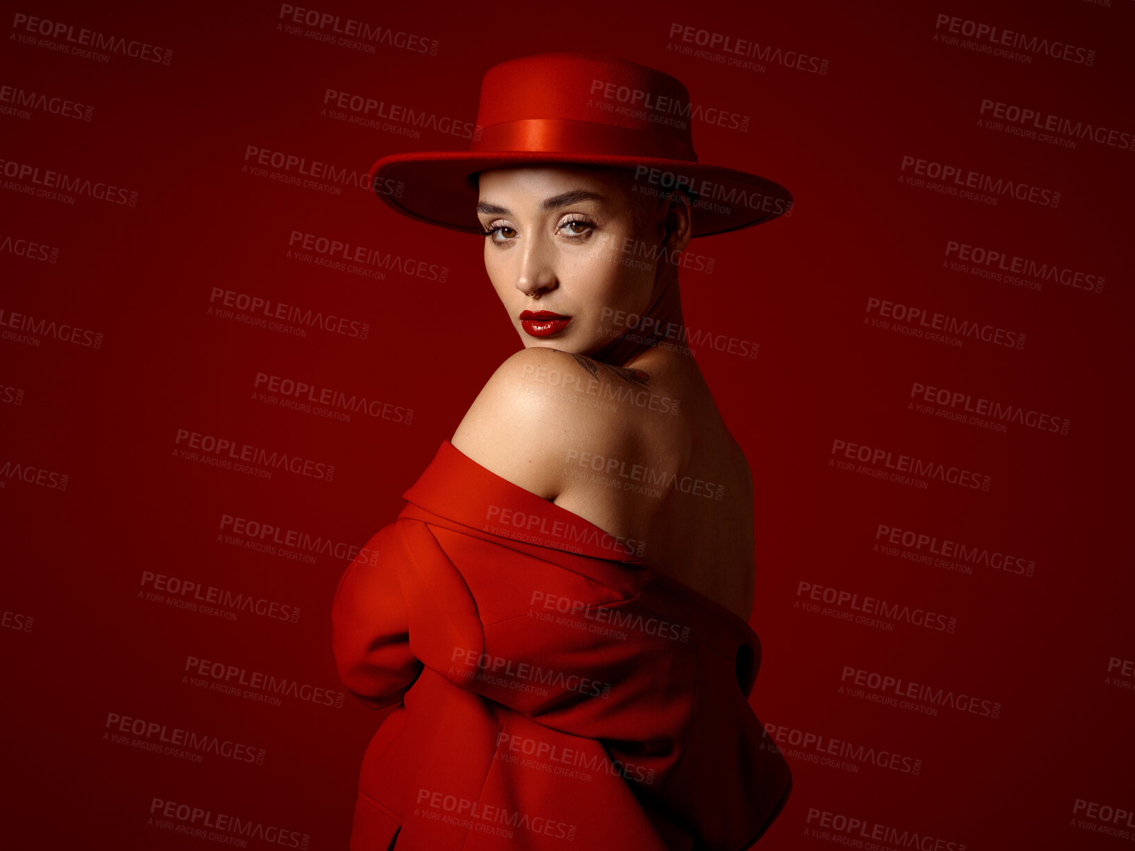 Buy stock photo Portrait, fashion and shoulder with a woman on a red studio background for elegant or trendy style. Aesthetic beauty, art and hat with a young female model looking edgy or classy in a unique outfit