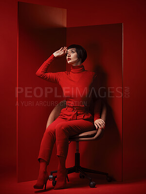 Buy stock photo Thinking, fashion and a model woman on red background in studio for elegant, chic or trendy style. Aesthetic, art and beauty with an edgy person in unique clothes suit, makeup and cosmetics on chair