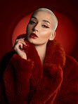 Fashion, portrait and serious woman in a red coat in studio isolated on a background. Face, makeup and confident bald model with cosmetics, aesthetic or style, trendy and fur clothes from Switzerland
