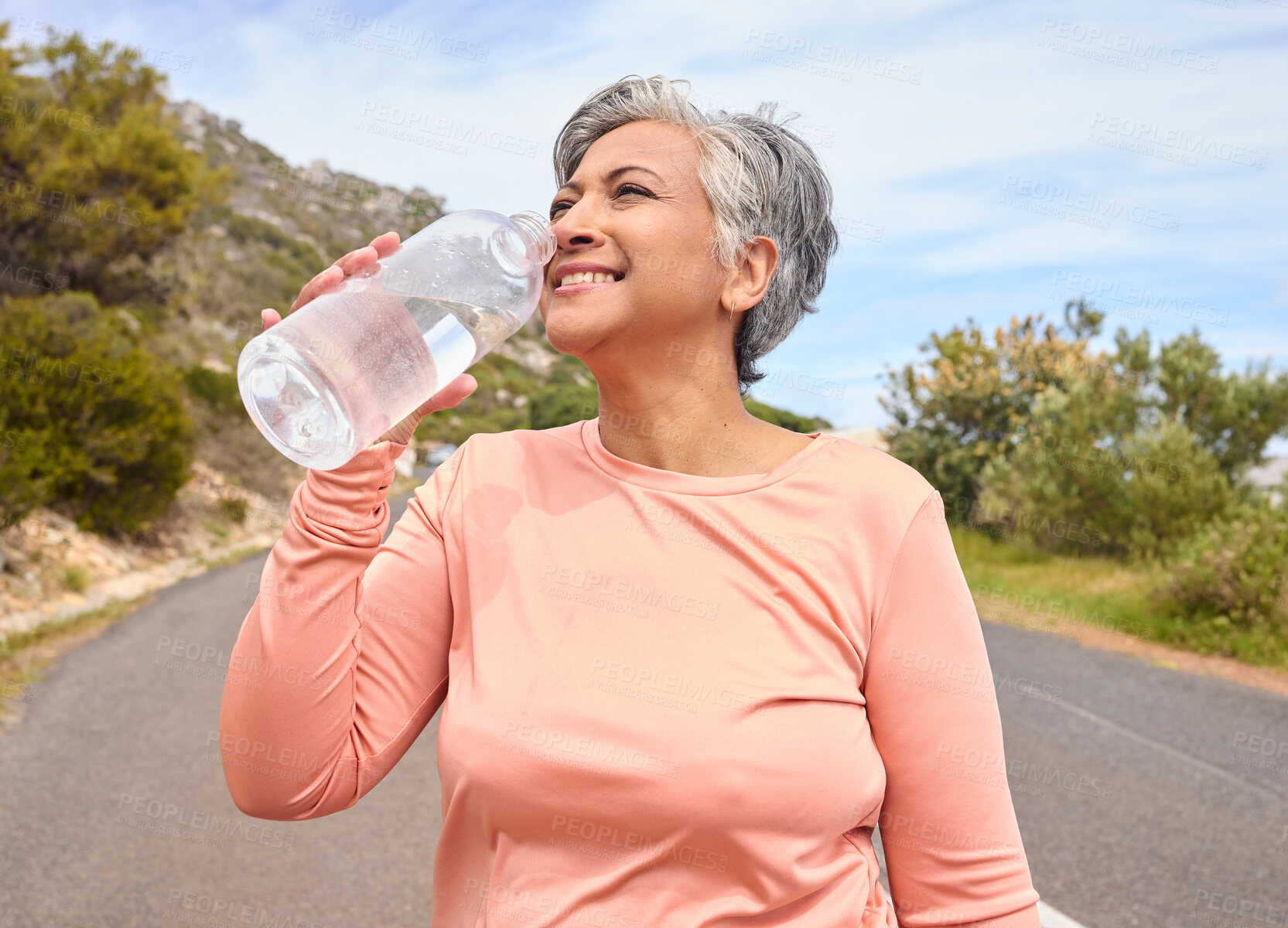 Buy stock photo Senior woman, drinking water and bottle on road for fitness, running and thinking of goal, hydration or health. Mature lady, runner and detox with smile for wellness, exercise or workout in nature