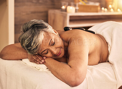 Buy stock photo Woman, spa and relax with stone massage on back for skincare treatment, holistic therapy and beauty salon. Mature female person at wellness resort with rocks for muscle healing, self care and peace