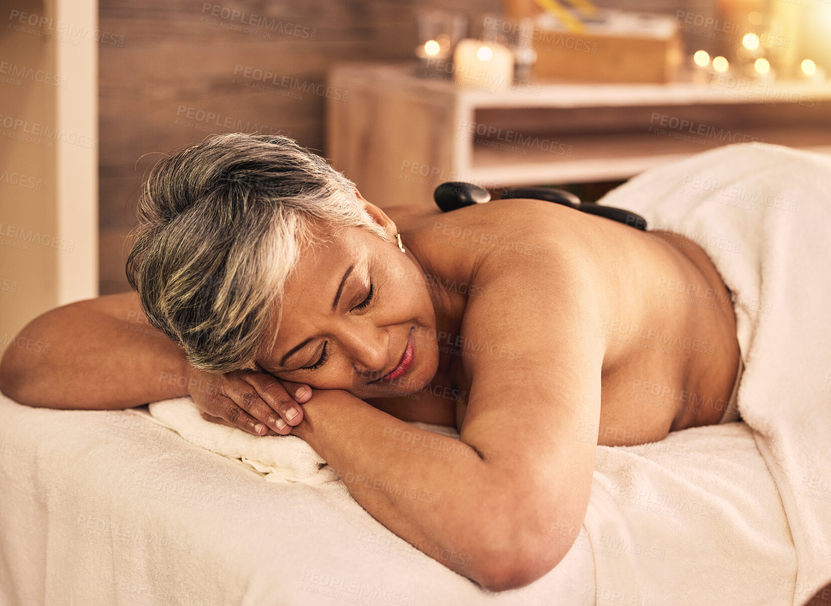 Buy stock photo Woman, spa and relax with stone massage on back for skincare treatment, holistic therapy and beauty salon. Mature female person at wellness resort with rocks for muscle healing, self care and peace