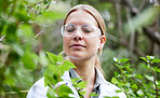 Scientist woman, plants and field research with focus, outdoor and glasses for safety, analysis and growth. Female science, forest or woods with leaves, plastic goggles or inspection for pharma study
