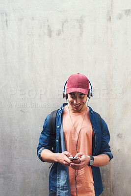 Buy stock photo Happy, headphones and man with phone on a wall for social media, communication or a chat. Smile, technology and a male college student streaming or listening to a podcast on a mobile app with mockup