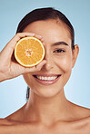 Happy woman, portrait and orange for vitamin C, diet or skincare against a blue studio background. Female person smile with organic citrus fruit for natural nutrition, dermatology or facial treatment