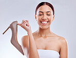 Fashion, smile and high heel with a model woman in studio on a gray background for footwear advertising.  Marketing, luxury or shopping with a happy young female customer holding a shoe for style