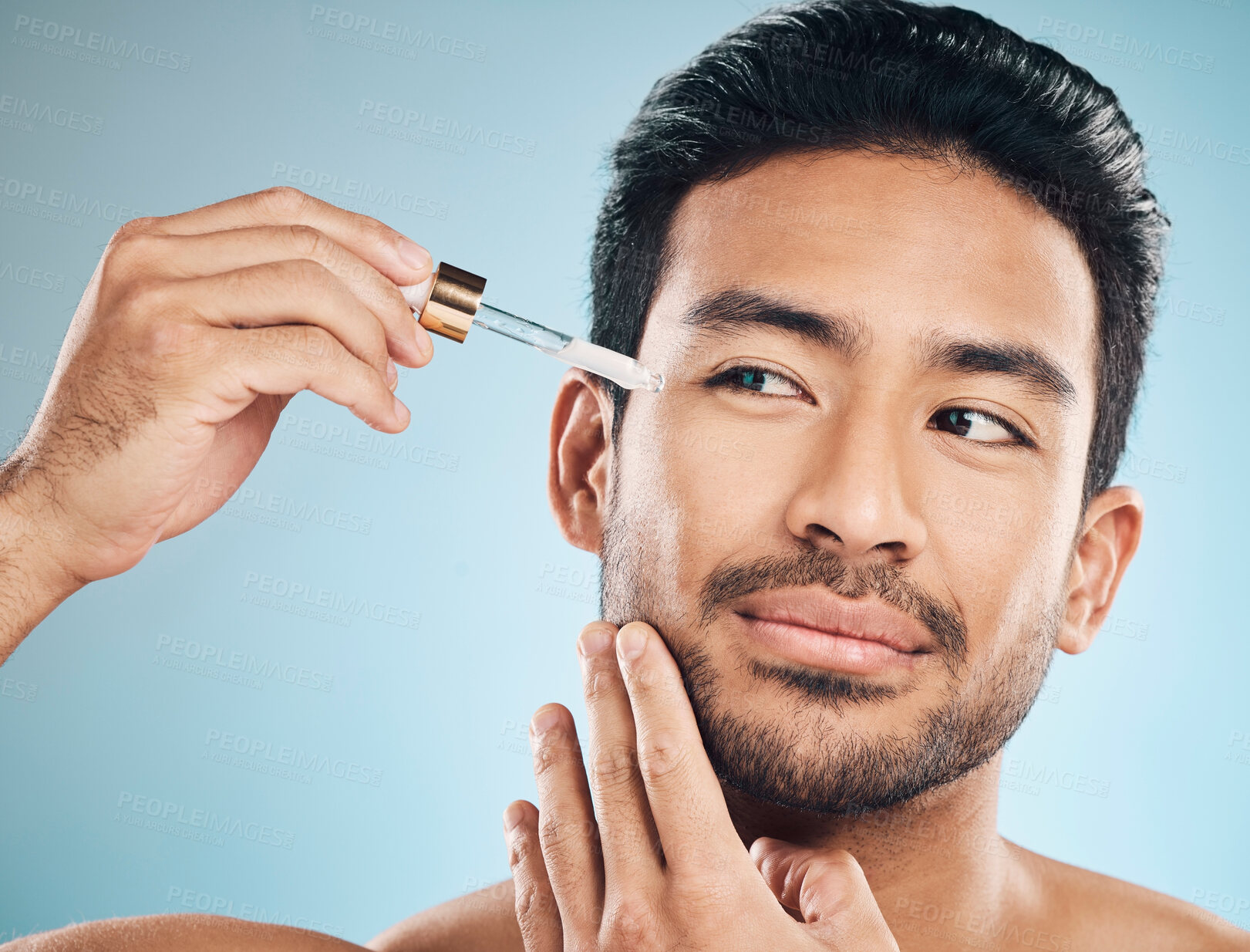 Buy stock photo Face, beauty and antiaging oil with a man in studio on a blue background for skincare or grooming. Luxury, serum or wellness with a handsome male person in the bathroom to apply a product to his face