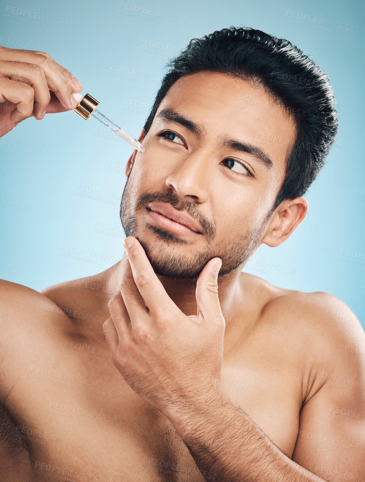 Buy stock photo Face, beauty and antiaging serum with a man in studio on a blue background for skincare or grooming. Luxury, oil or wellness with a handsome male person in the bathroom to apply a product to his skin