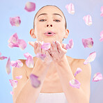 Woman, portrait and blowing petals for beauty, natural skincare and facial glow of eco cosmetics in studio. Face, female model and pink flowers in hands for sustainable dermatology on blue background