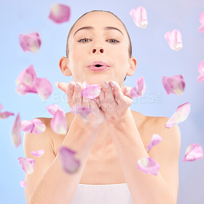 Buy stock photo Woman, portrait and blowing petals for beauty, natural skincare and facial glow of eco cosmetics in studio. Face, female model and pink flowers in hands for sustainable dermatology on blue background