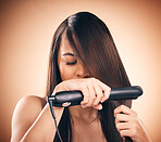 Young woman, hair care and flat iron in studio to straightener for healthy shine and growth. Young female aesthetic model on a brown background with hot tools for hairstyle, cosmetics and beauty 