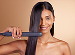 Portrait, hair and straightener with a model woman in studio on a beige background for beauty or style. Face, smile and haircare with happy young person using a flat iron appliance for natural care