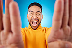 Selfie, excited and portrait of a man in studio with hands and shout emoji. Face of asian male or fashion model on blue background with surprise and fun energy for social media profile picture update