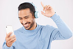Headphones, phone and man dancing in a studio with music, album or playlist with technology. Happy, smile and Indian young male person doing a dance to song or radio isolated by a white background.