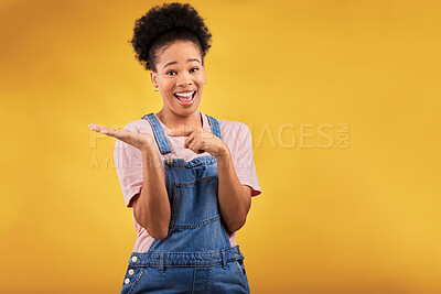 Buy stock photo Portrait, space and a black woman pointing to her palm for the promotion of a product on a yellow background in studio. Smile, advertising or marketing with a happy young female brand ambassador