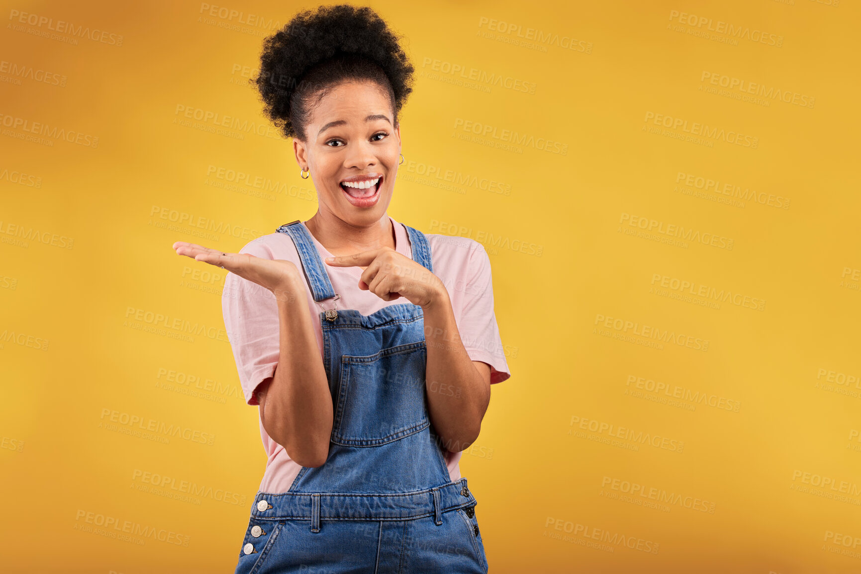 Buy stock photo Portrait, space and a black woman pointing to her palm for the promotion of a product on a yellow background in studio. Smile, advertising or marketing with a happy young female brand ambassador