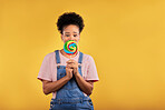 Black woman, portrait with candy or lollipop in studio on yellow background and eating sweets, dessert or food with sugar. Gen z, girl and guilty pleasure in delicious treats, snack or product