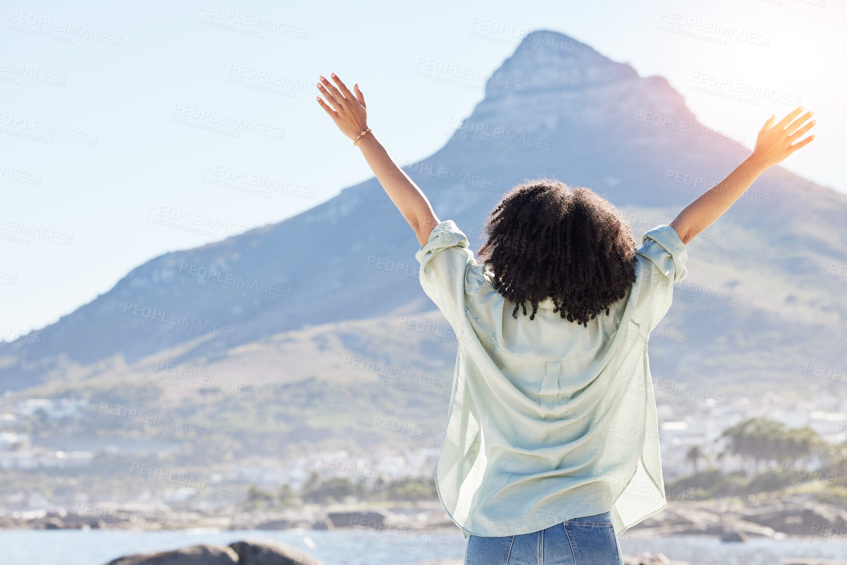 Buy stock photo Woman at beach, arms in air and freedom, back view with mountains and travel, praise and sunshine. Female person outdoor, carefree and adventure, mindfulness and peace with worship in nature
