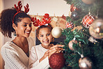 Christmas, portrait and mother with girl decorating tree, bonding and happy together. Xmas, smile and face of kid with African mom with ornament for family party, celebration or holiday event in home