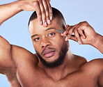 Self care, tweezer and portrait of a man in a studio grooming and shaping his eyebrows for epilation. Beauty, hygiene and young male model with face hair removal treatment isolated by blue background