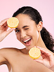 Woman, beauty and lemon for wink in studio portrait, smile and natural skin glow by pink background. Latino girl, model and fruit for cosmetics, eye emoji and detox for wellness, nutrition and shine
