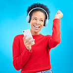 Happy woman, headphones and listening to music for audio streaming against a blue studio background. Excited female person dancing and enjoying sound track or entertainment with mobile smartphone