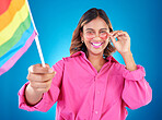 Woman, lgbtq and pride flag in studio portrait, sunglasses or icon with smile for human rights by blue background. Gen z girl, young lesbian student and wave sign for solidarity, freedom or inclusion