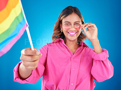 Buy stock photo Woman, lgbtq and pride flag in studio portrait, sunglasses or icon with smile for human rights by blue background. Gen z girl, young lesbian student and wave sign for solidarity, freedom or inclusion