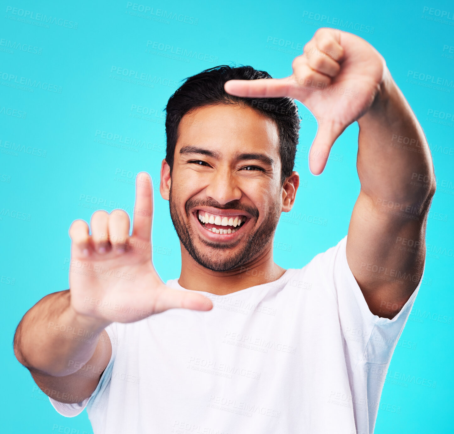 Buy stock photo Happy, hand frame and portrait of a man for a selfie, creative aesthetic or advertising photography. Smile, laughing and face of an Asian person with a gesture for a photo on a blue background