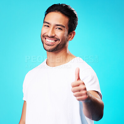 Buy stock photo Smile, thumbs up and portrait of a man in a studio with a satisfaction sign or expression. Happy, emoji and young Indian male model with an agreement hand gesture isolated by a blue background.