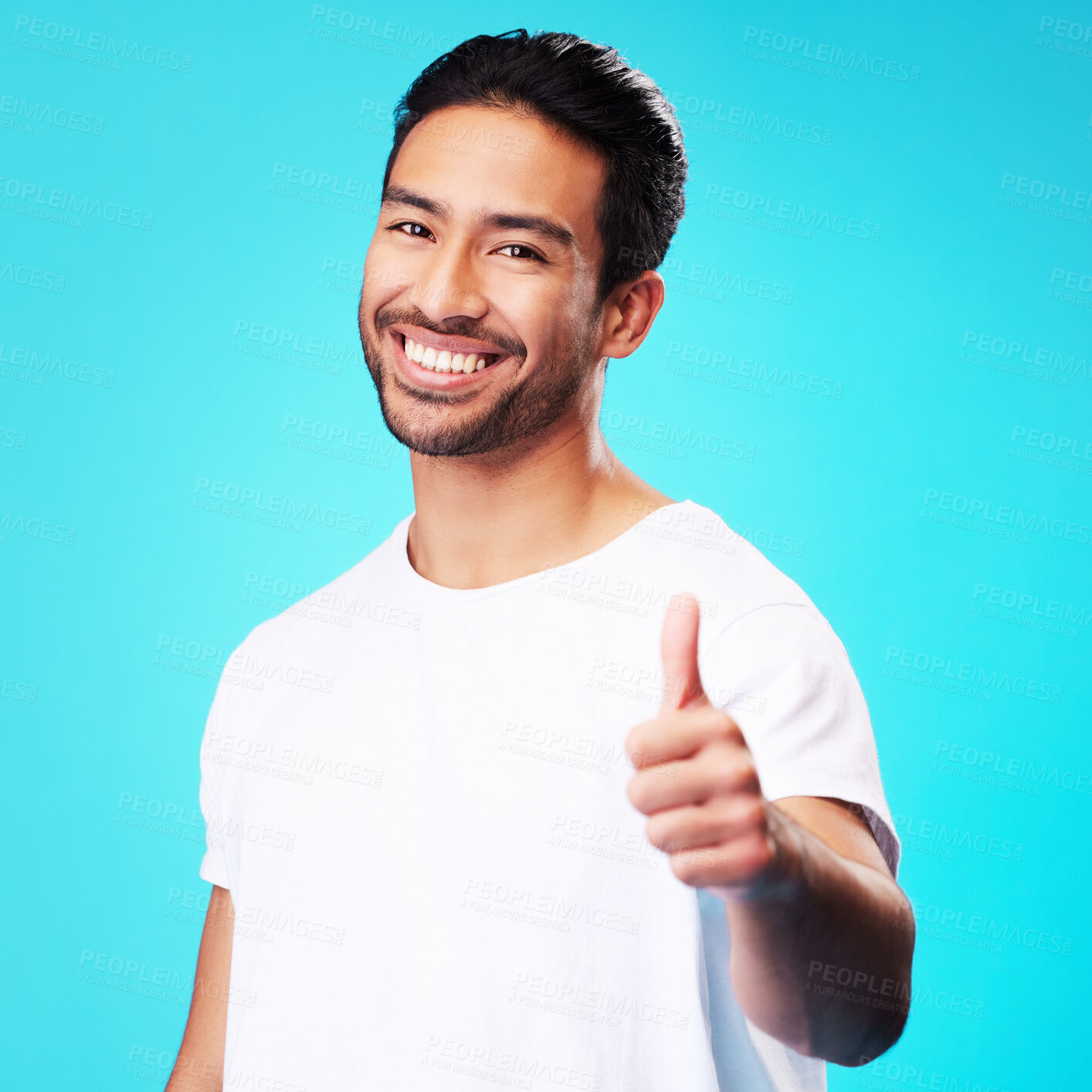 Buy stock photo Smile, thumbs up and portrait of a man in a studio with a satisfaction sign or expression. Happy, emoji and young Indian male model with an agreement hand gesture isolated by a blue background.