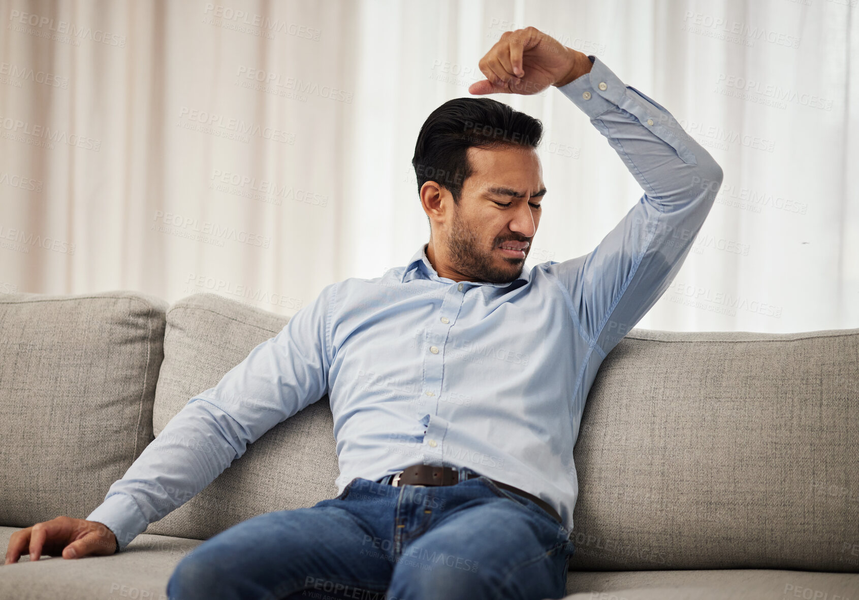 Buy stock photo Armpit stink, smelling and a man on the sofa with a hygiene or bacteria problem. Bad, home and an Asian person with body odor, underarm sweat or grooming issue on the living room couch after work