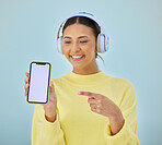 Happy woman, phone mockup and pointing for advertising or marketing against a studio background. Female person smile and listening to music on headphones with mobile smartphone app display or screen