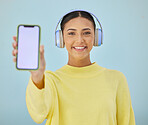 Portrait of happy woman with phone screen, headphones and mockup in studio for social media, mobile app and streaming radio. Smile, music subscription and girl with cellphone on blue background space