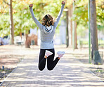 Fitness, jump and a woman outdoor with hands raised at a park for celebration, win and success. Back of young female person on a road in nature excited about workout, running or training goals
