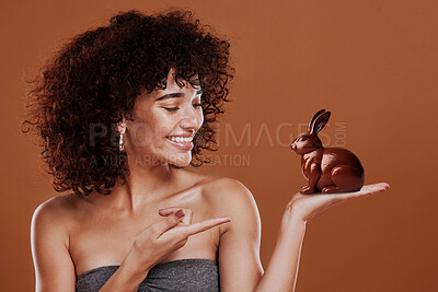 Chocolate, candy and bunny with woman and pointing in studio for easter, sweets or sugar. Cocoa, food and confectionery with face of person and treat on brown background for holiday, mockup and space