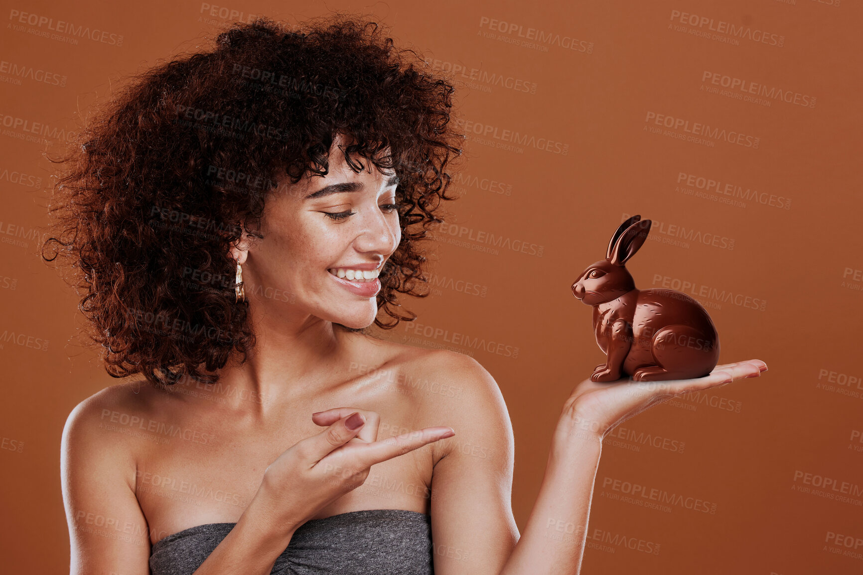 Buy stock photo Chocolate, candy and bunny with woman and pointing in studio for easter, sweets or sugar. Cocoa, food and confectionery with face of person and treat on brown background for holiday, mockup and space
