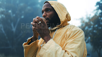 Coffee, morning and black man hiking in the forest with a blurred background of cold, winter weather. Thinking, raincoat and face of a young male hiker in the woods or nature to explore for adventure