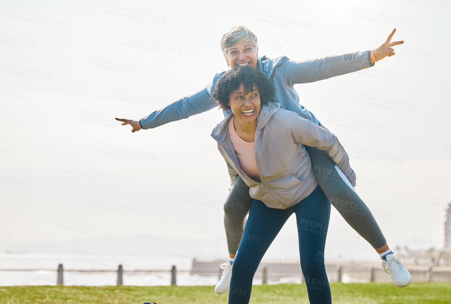 Buy stock photo Beach, funny and senior friends piggyback together doing airplane gesture playing, crazy and laughing at outdoor exercise. Health, wellness and goofy elderly women bonding by the sea for workout