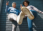 Bottom view, shoes and women with portrait, peace sign and smile outdoor. Wall, mature female friends and urban fitness feet with exercise sneakers, fashion and happy, v and emoji hand gesture
