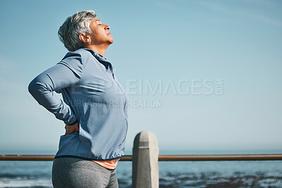 Buy stock photo Tired, running and senior woman pain from back ache by the ocean for fitness, exercise and workout. Runner, person with sport outdoor on beach with muscle strain and athlete injury on mockup space