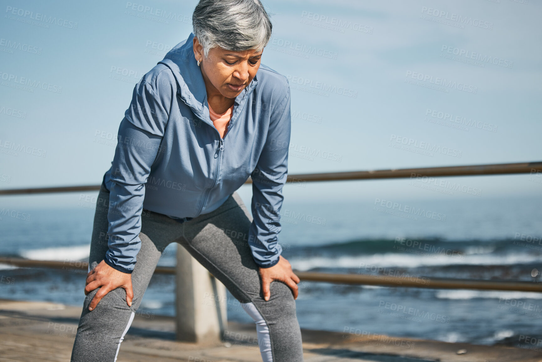 Buy stock photo Senior, exercise and tired woman at the beach on break from training, workout or morning cardio run in nature. Sports, fatigue and elderly female runner stop to breathe on ocean workout or fitness