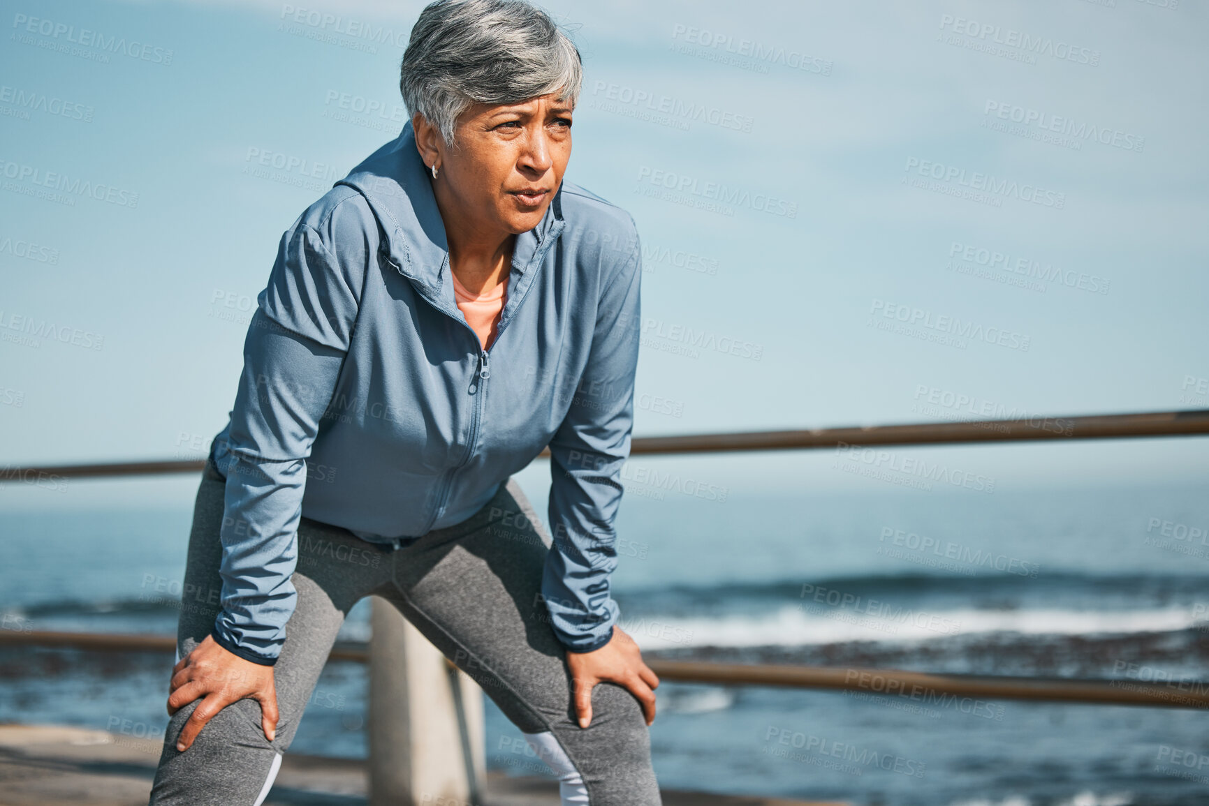 Buy stock photo Senior, fitness and tired woman at the beach on break from training, workout or morning cardio run in nature. Sports, fatigue and elderly female runner stop to breathe on ocean workout or performance