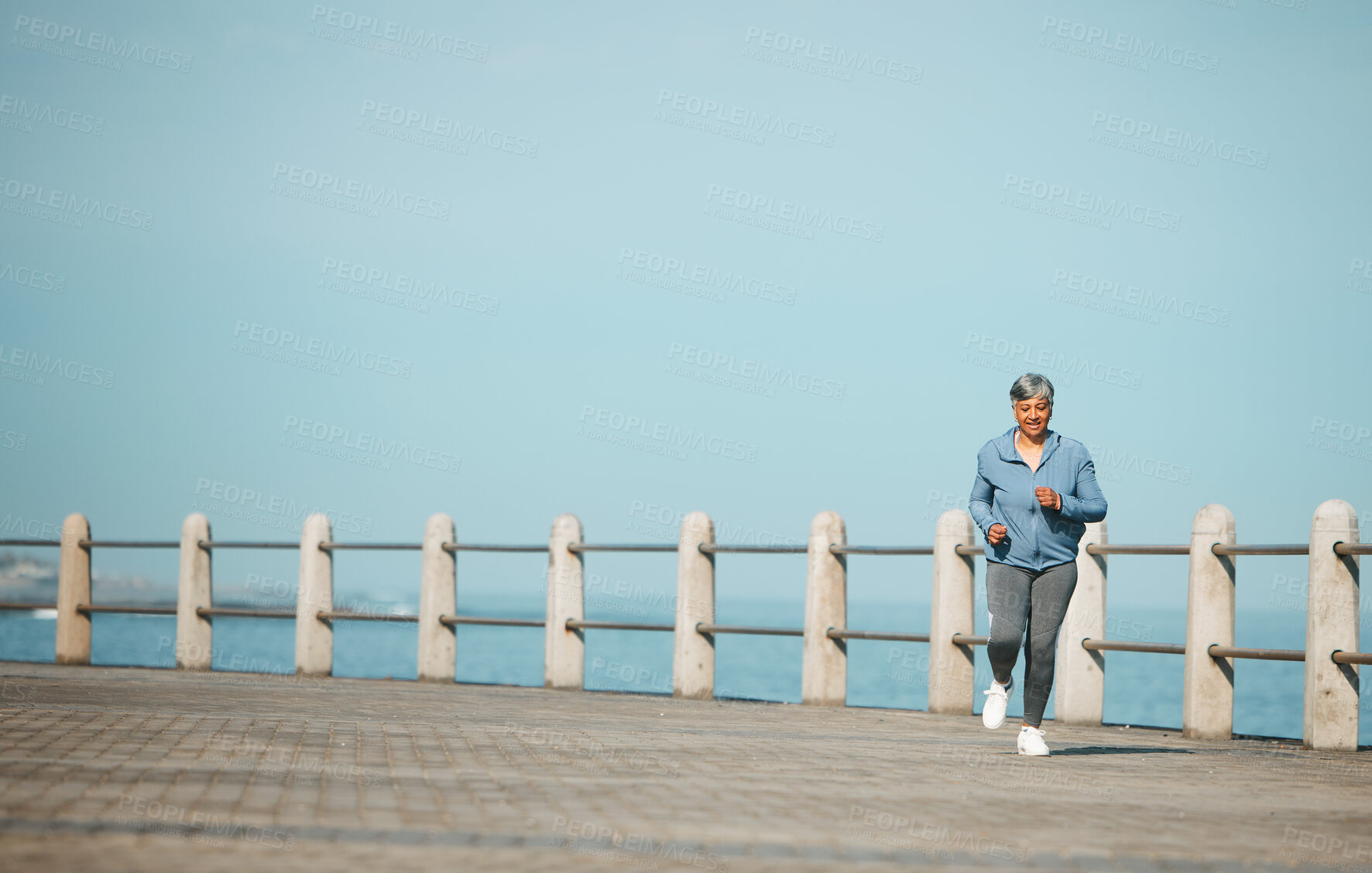 Buy stock photo Fitness, running and senior woman at the beach for exercise, health or cardio on blue sky background. Training, wellness and elderly female runner at the sea for morning workout, routine or ocean run